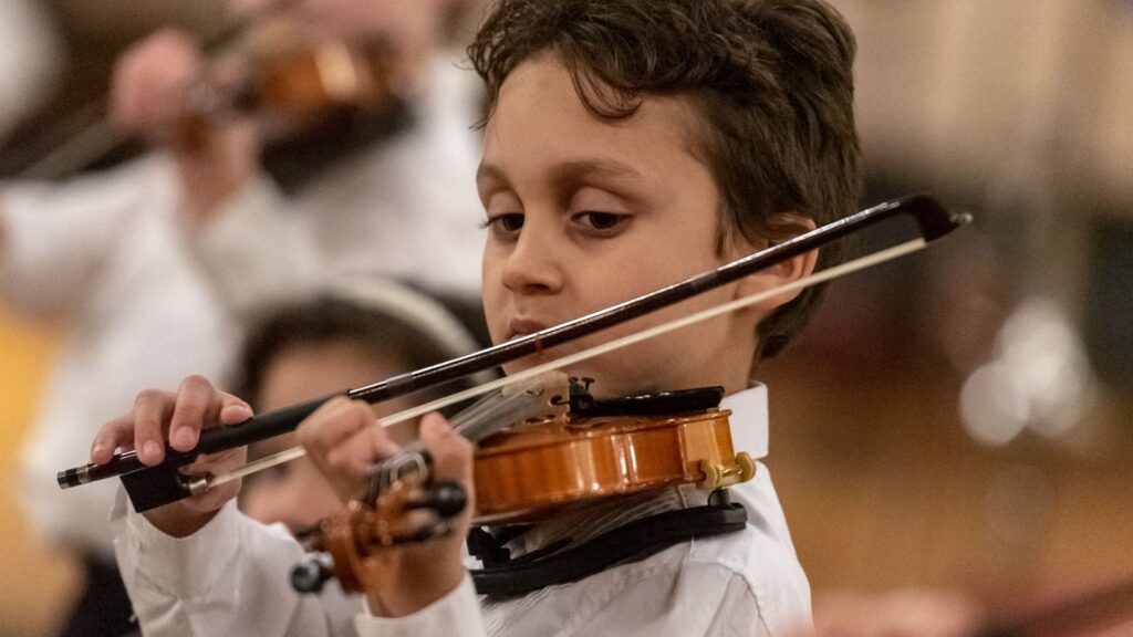Young boy plays violin as part of Suzuki program concert.